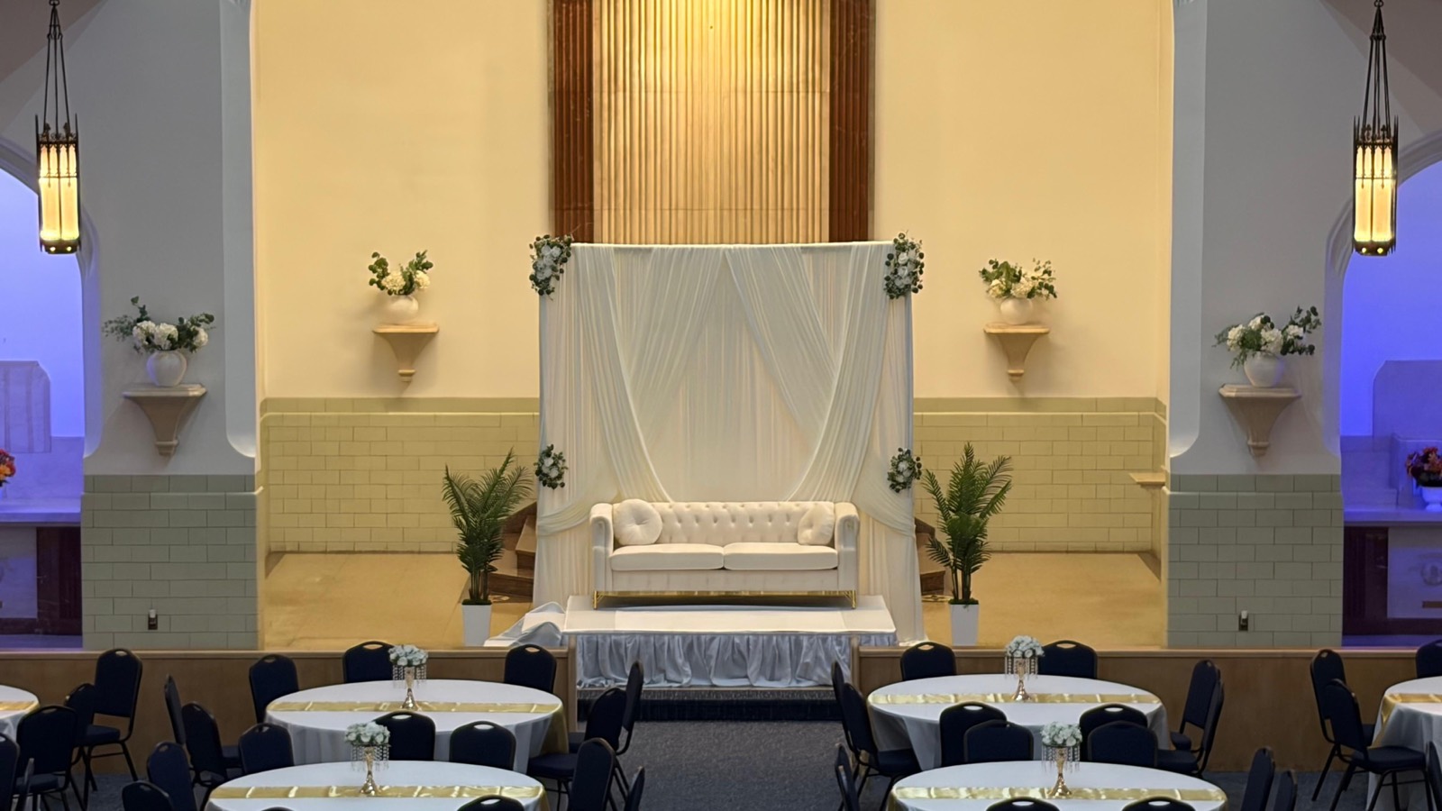 A draped stage backdrop set with florals and soft uplighting